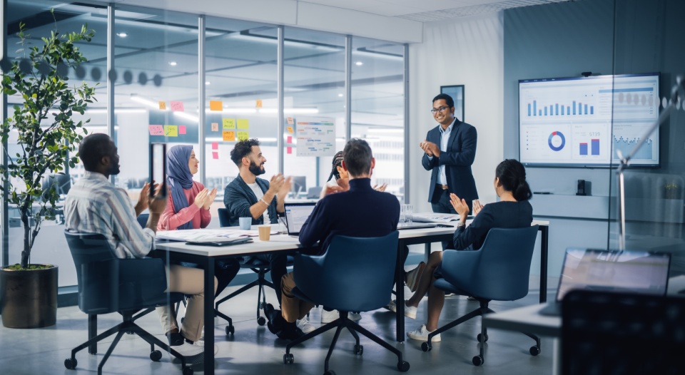 Multi-Ethnic Office Conference Room. Indian CEO does Presentation for Diverse Young Entrepreneurs, Talking, Using TV with Infographics, Statistics, Graphs. Businesspeople Invest in e-Commerce Startup